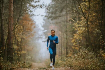 دانلود عکس زن جوان در حال دویدن به سمت دوربین در مسیر جنگل در پاییز