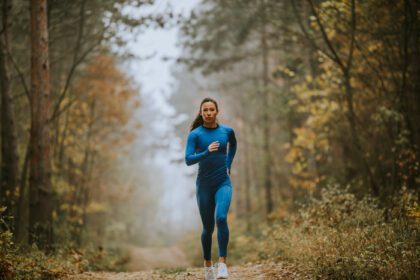 دانلود عکس زن جوان در حال دویدن به سمت دوربین در مسیر جنگل در پاییز