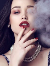 دانلود عکس آتلیه مد عکس زن زیبا با موهای تیره و آرایش روشن با ژست بیژو در دود سیگار