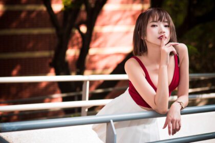 دانلود والپیپر زنان آسیایی مدل عمق میدان نرده رژ لب قرمز ساعت سبزه تاپ قرمز دامن سفید انگشت روی لب درختان
