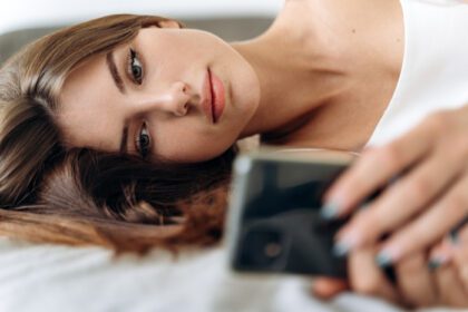 دانلود عکس زنی که روی تختش دراز کشیده به تلفن همراه نگاه می کند