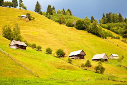 دانلود عکس منظره کوه در moeciu de sus romania با کابین های چوبی بر روی تپه های سبز