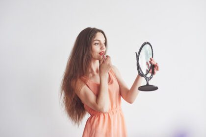دانلود عکس زن جوان زیبا که آینه ای در دست دارد و در حال آرایش است