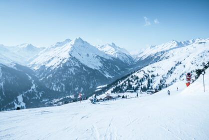 دانلود عکس اسکی بازان در حال اسکی روی شیب کوه پوشیده از برف در مقابل آسمان آبی
